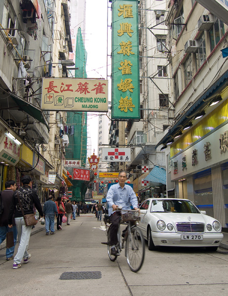 De man fietst door één van de drukke marktstraatjes die het Tsim-Tsa-Tsui deel van Kowloon, Hong Kong, rijk is.